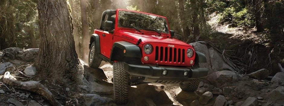 A red 2018 Jeep Wrangler driving through a rocky forest